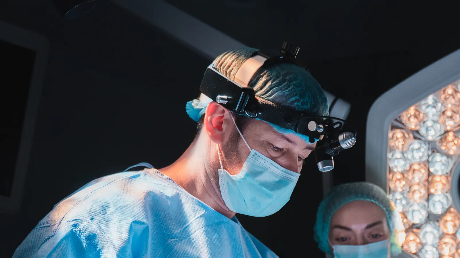 A surgeon in a mask and headlamp concentrating during an operation
