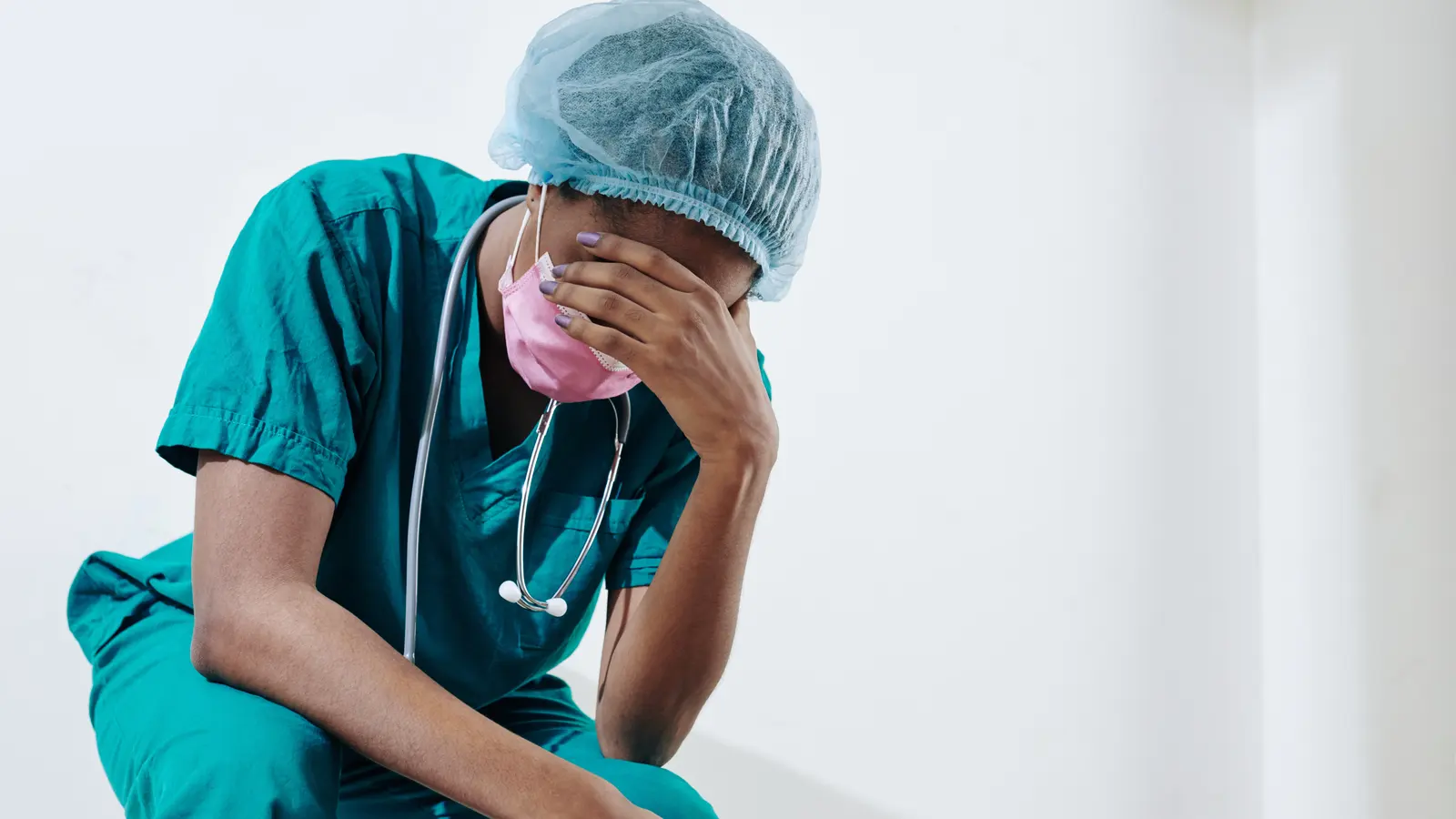 A healthcare worker in scrubs sitting with their head in their hand