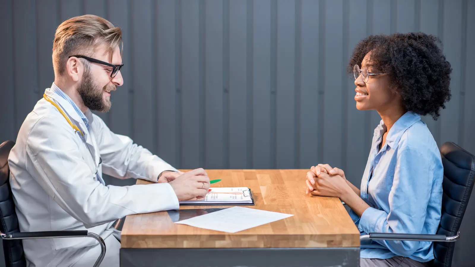 A clinician in a white coat and an applicant seated across a table in conversation